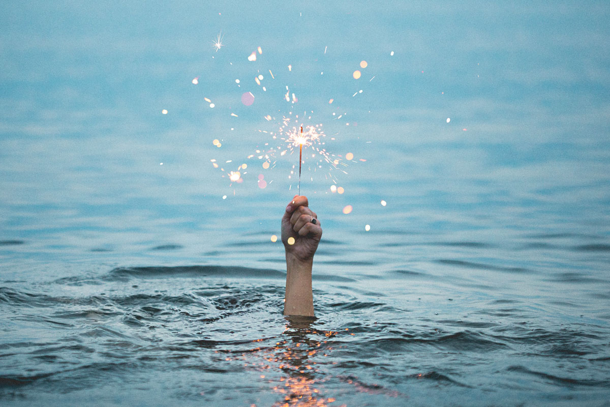 image of a hand holding a lit sparkler out of the water